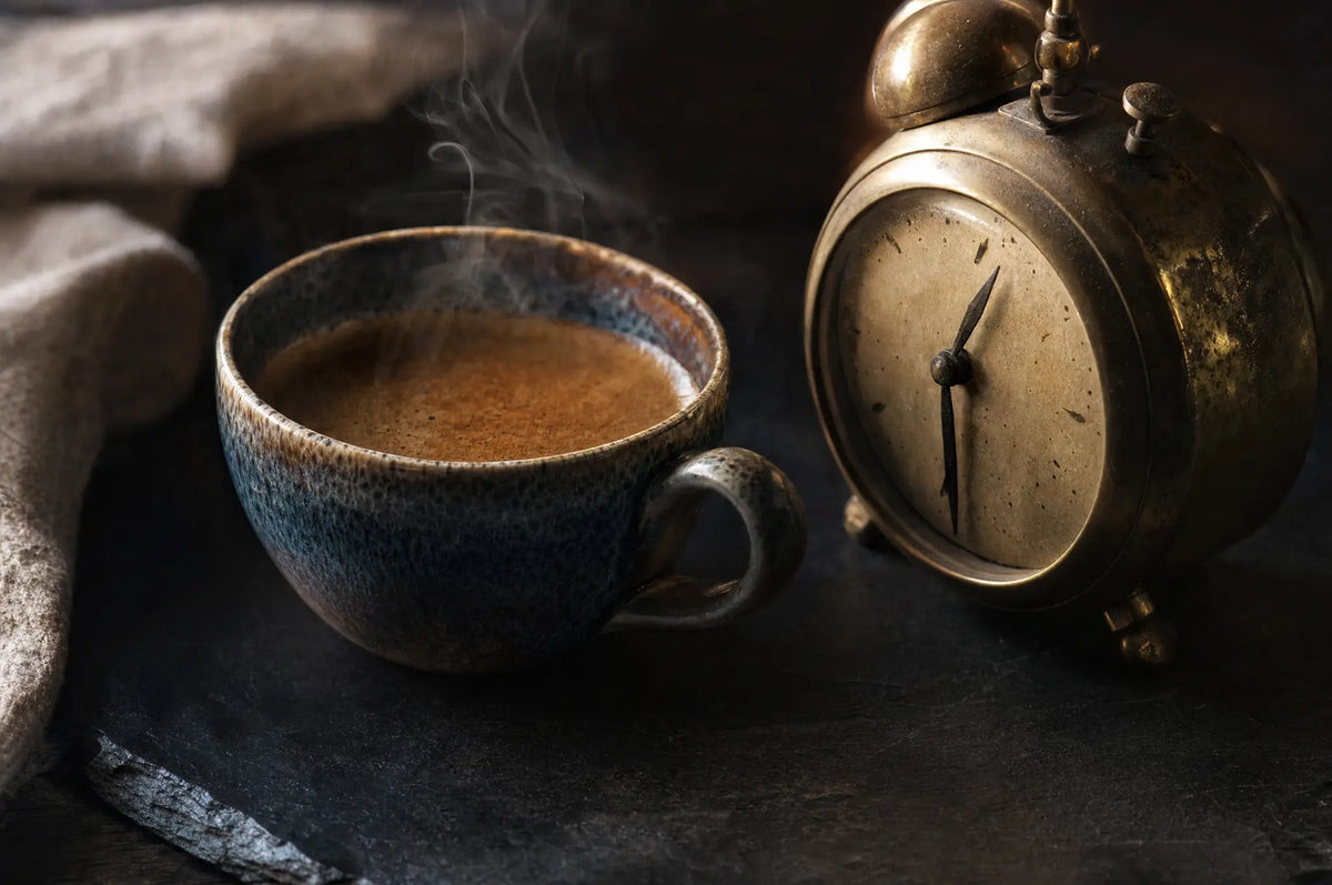 Caffeine Timing: Do You Really Need to Wait 90 Minutes After Waking? — A single espresso cup with a thin stream of steam rising, resting on a dark slate surface beside an old brass 