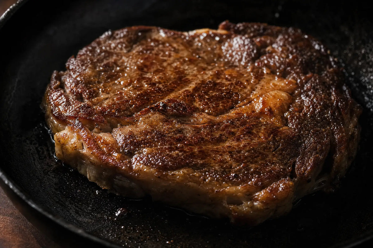 Does Chronic Stress Make You Burn Muscle Instead of Fat? The Claim Is Too Simple — A raw grass-fed ribeye steak, seared and glistening with juices, resting on a blackened cast iron skillet with