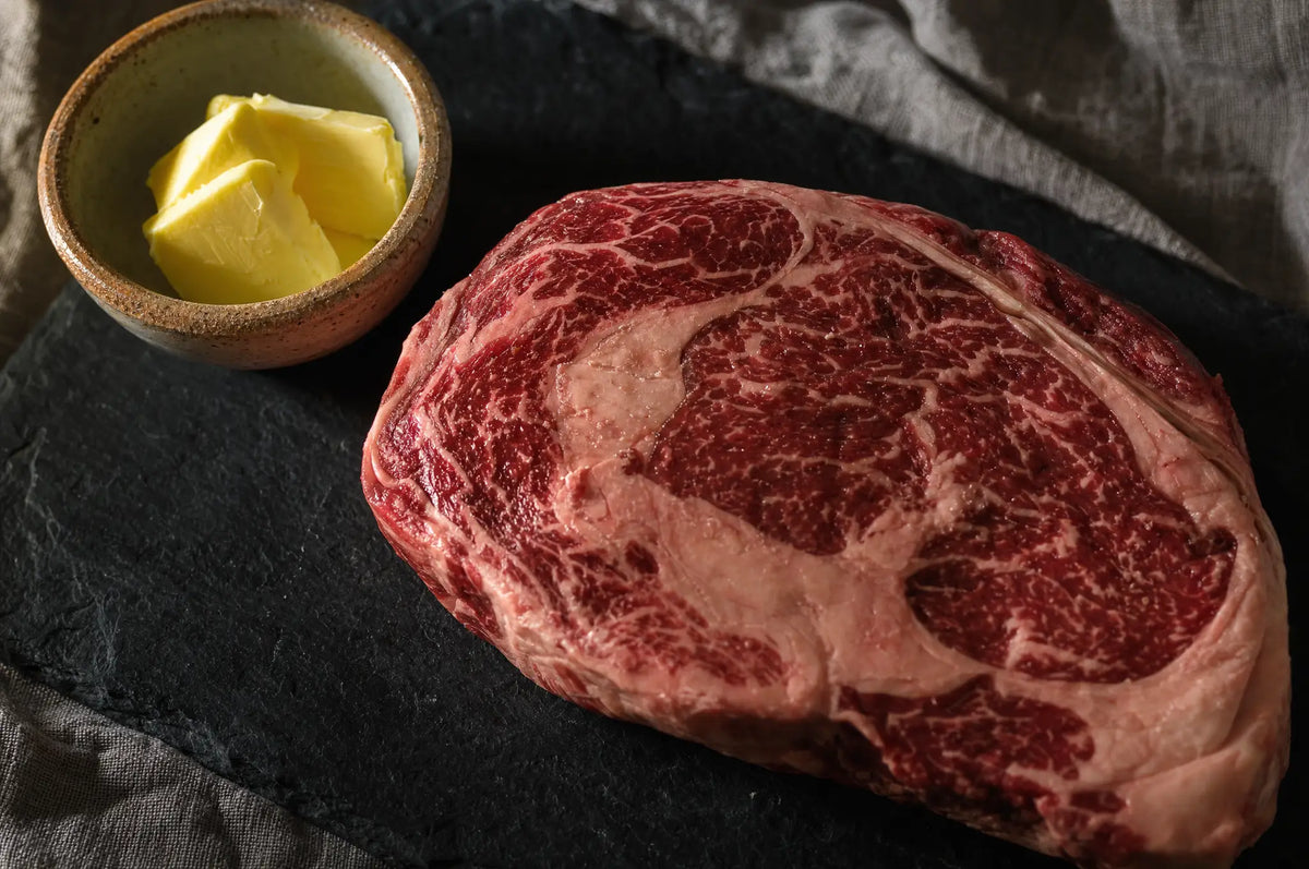 Why Extreme Dieting Gets Harder: Appetite, Adaptation, and the “Hoard Fat” Myth — A single cold ribeye steak rests on a dark slate board beside a small ramekin of pats of golden butter, lit by