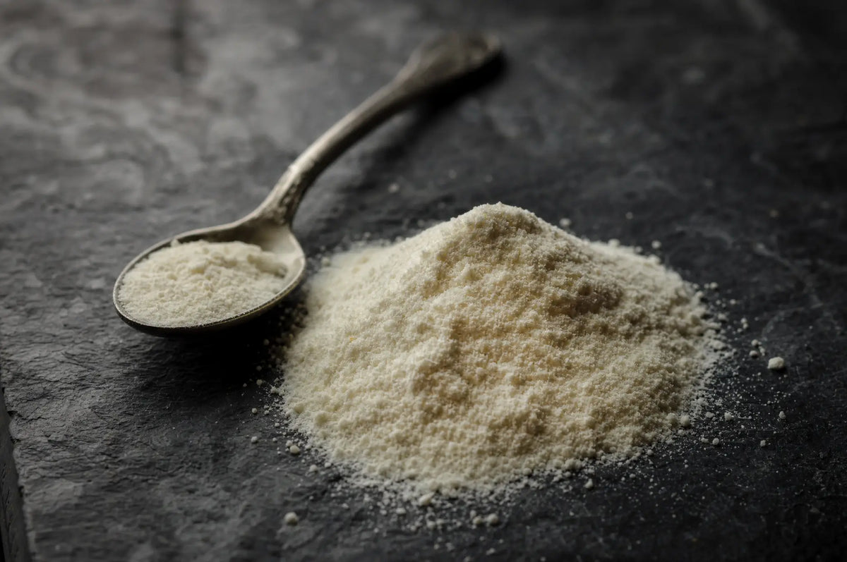 Is Collagen Effective? Results From 2026 Clinical Trials — A small pile of loose collagen peptide powder resting on a dark slate surface beside a spoon, lit softly from 