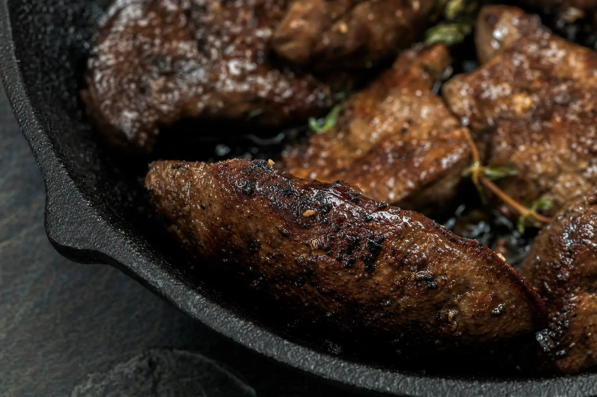 Cast-iron skillet with seared beef liver on dark slate, one crisp edge in sharp focus