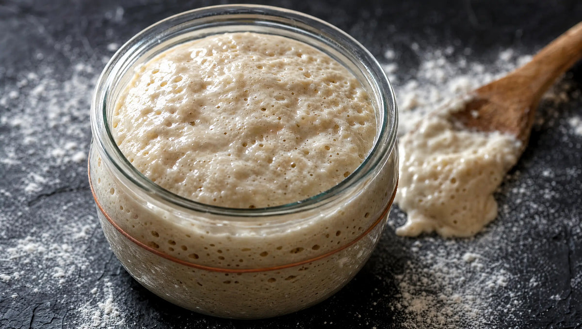 A glass jar of bubbly active sourdough starter on dark slate