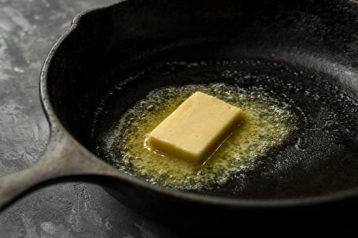 Seed Oils, Oxygen, and Thyroid Health: What the Evidence Actually Supports — A pat of butter melting in a blackened cast iron skillet on a dark slate surface.