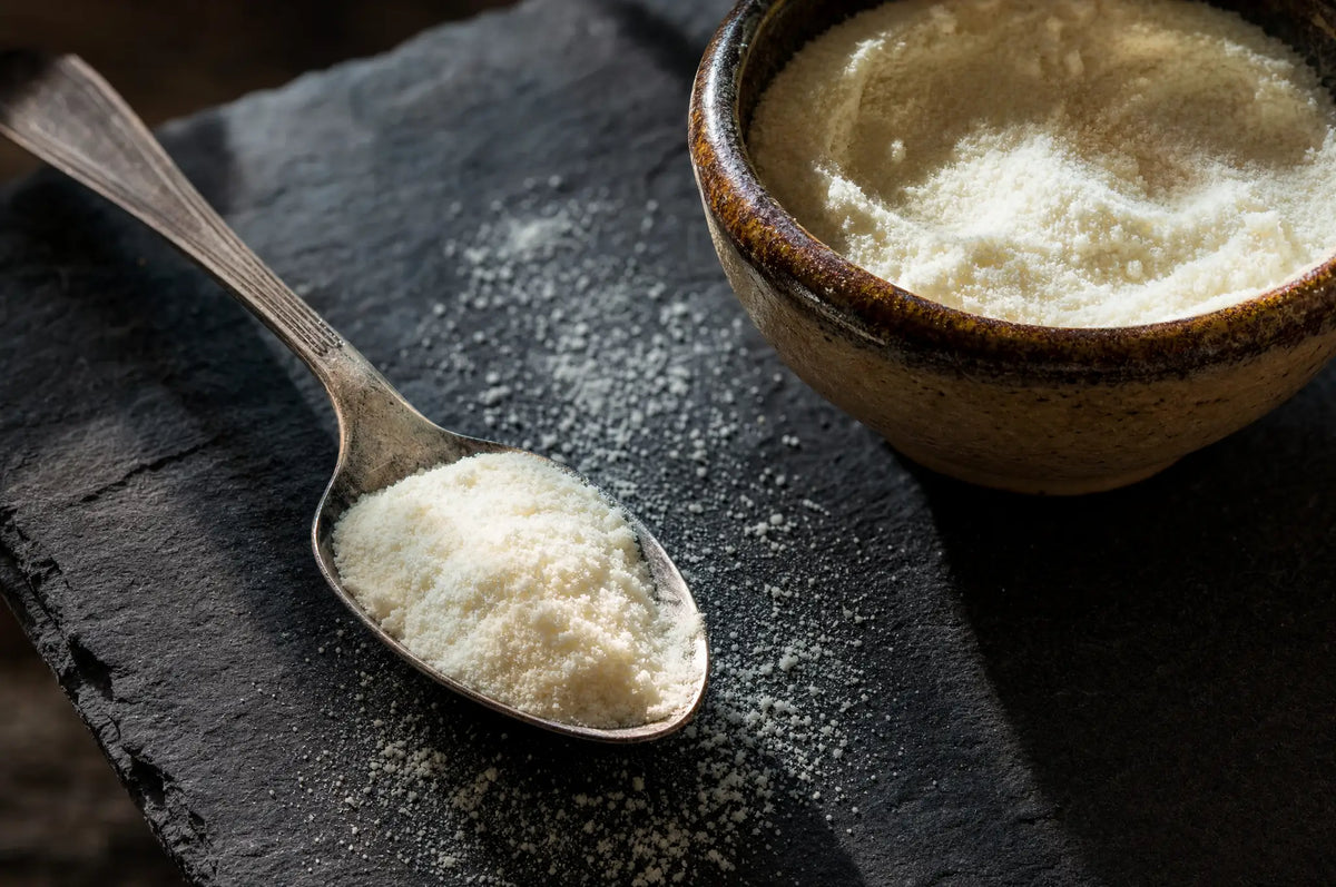 The Benefits of Collagen as a Dietary Supplement — A spoonful of pale collagen powder resting on a dark slate surface, with a small glazed stoneware bowl of the 