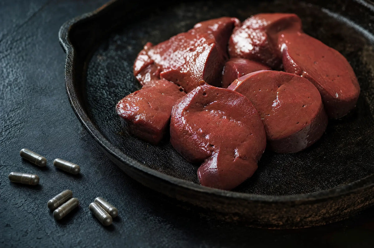 Raw beef liver medallions on a blackened cast iron skillet with loose zinc capsules on dark slate